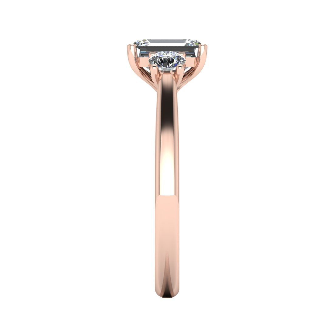 side view of a trilogy rose gold engagement ring set with an emerald centre lab grown diamond with two round brilliant diamonds on either side of the centre stone