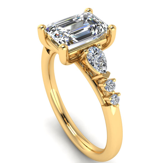angled view of yellow gold engagement ring. There is a emerald cut centre lab grown diamond with an arrangement of pear shaped and round diamonds on each side