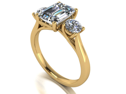 angled view of a trilogy yellow gold engagement ring set with an emerald centre lab grown diamond with two round brilliant diamonds on either side of the centre stone