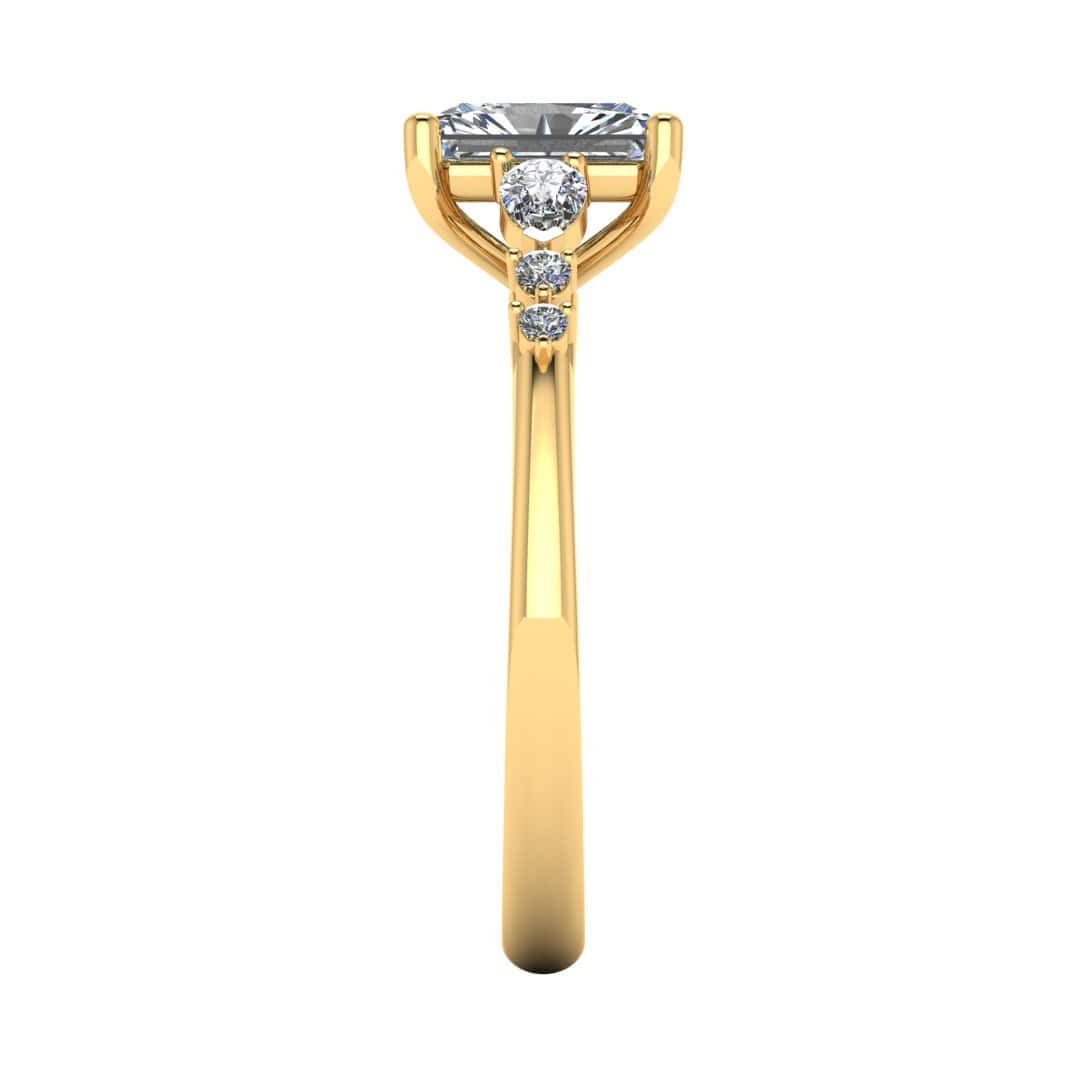 side view of a yellow gold multi-stone lab grown diamond engagement ring. It features a radiant cut lab-grown diamond with one pear and two round side diamonds on either side